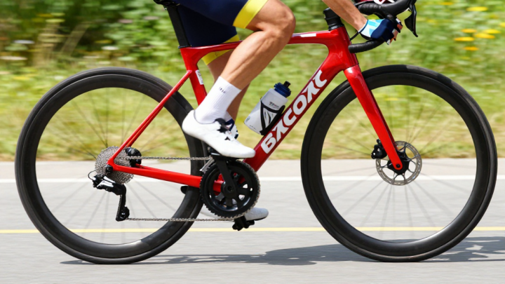 Piernas de un ciclista pedaleando en carretera, rueda en movimiento, luz brillante