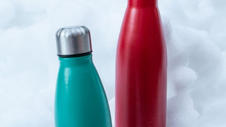 Dos bidones térmicos, uno verde azulado y otro rojo, sobre nieve fresca
