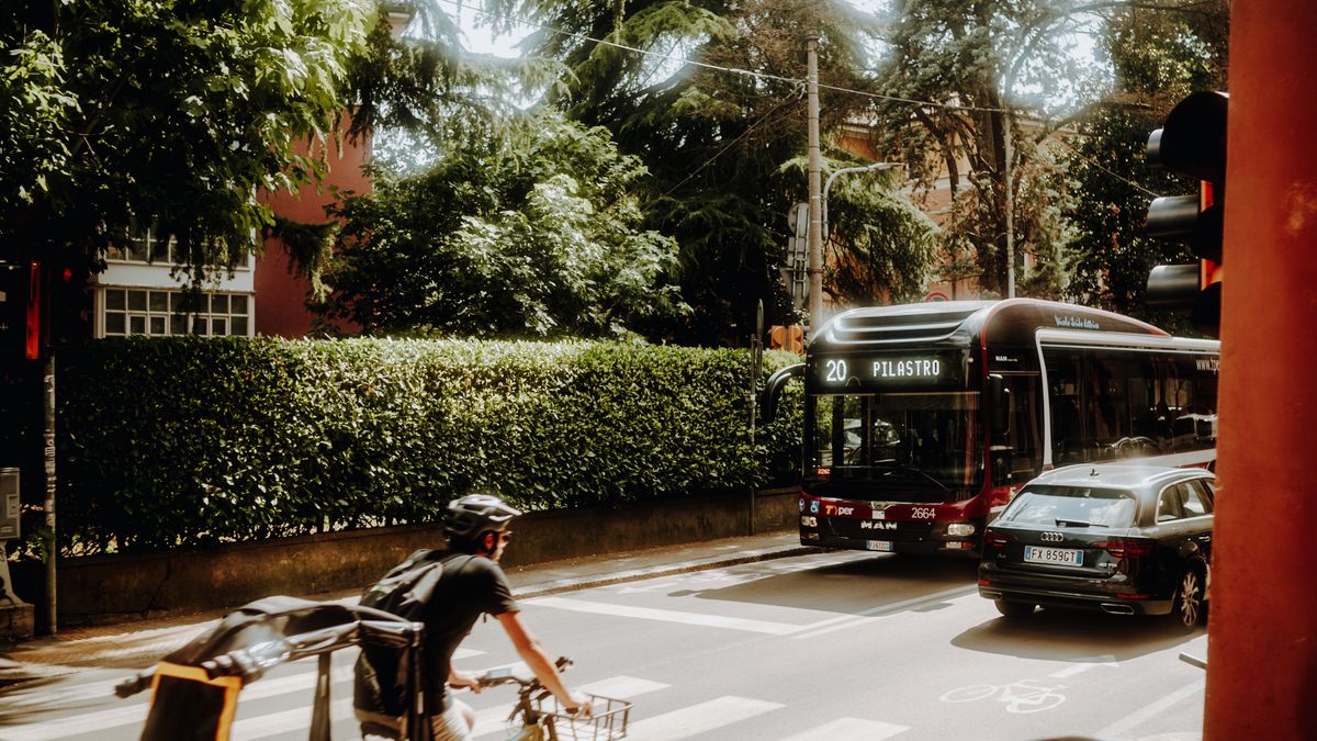 Ciclista esperando en un cruce urbano con un autobús y coches aproximándose por detrás