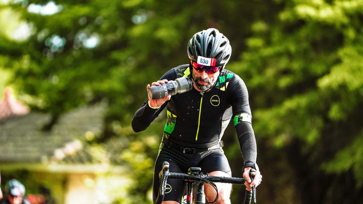 Ciclista bebiendo de un bidón en pleno esfuerzo bajo el sol, rodeado de vegetación