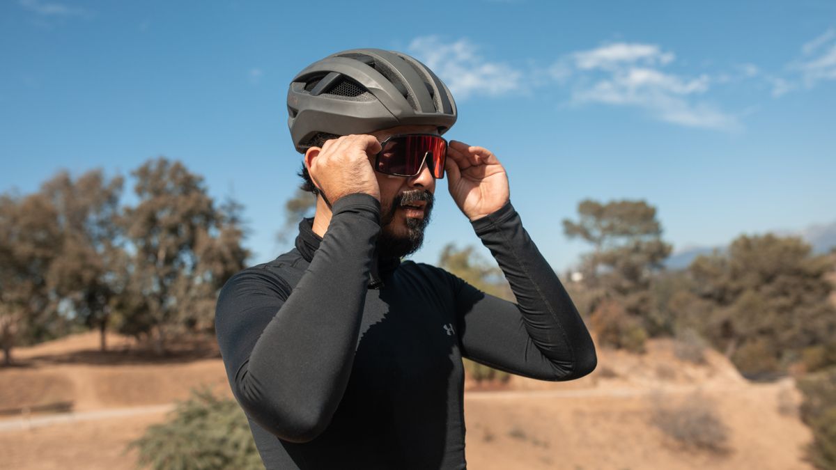 Ciclista con maillot de manga larga ajustándose las gafas de sol bajo un sol intenso