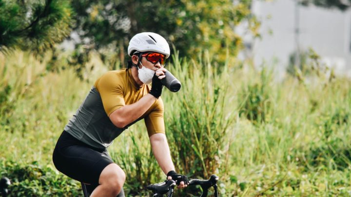 Ciclista con maillot amarillo bebiendo de un bidón en una ruta rodeada de vegetación en verano